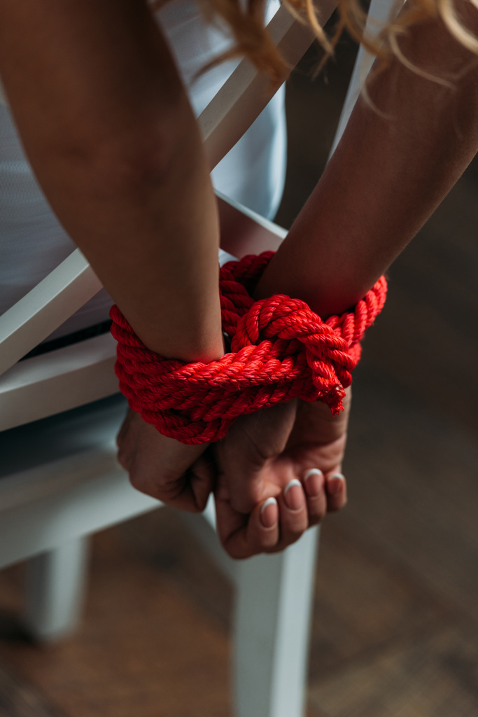 Vista recortada de las manos femeninas atadas con cuerda roja sobre fondo de madera
 - Foto, imagen