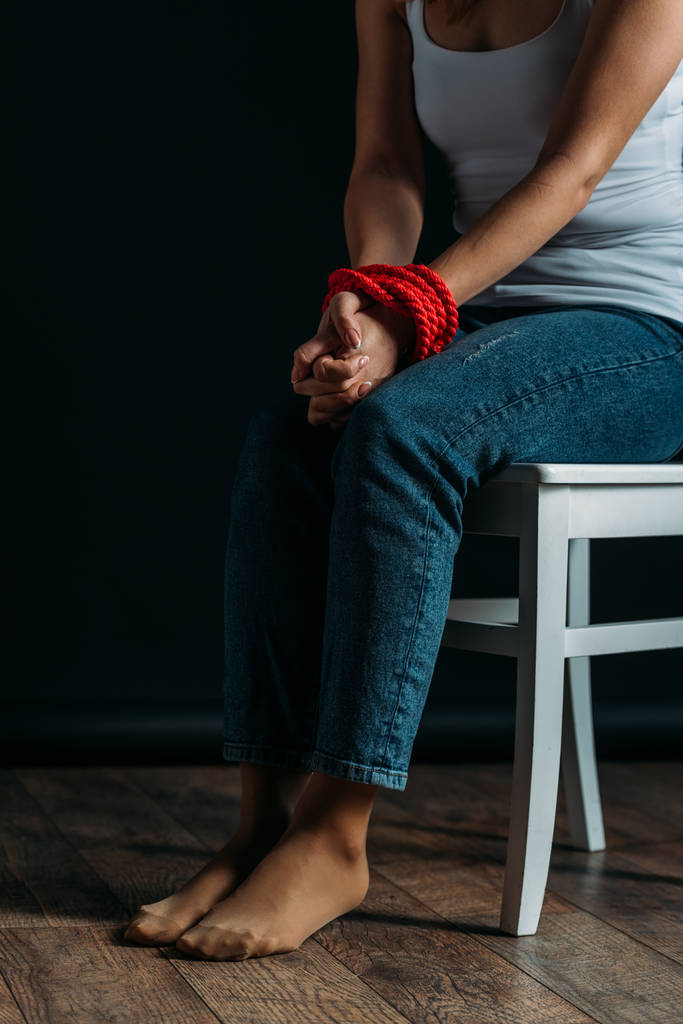 Cropped view of woman with tied hands sitting on chair on black background - Photo, Image