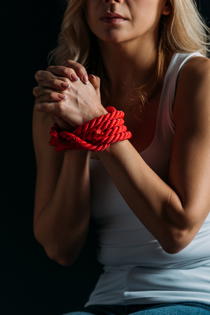 Vista parcial de las manos de mujer atadas con cuerda roja aislada en negro
  - Foto, imagen