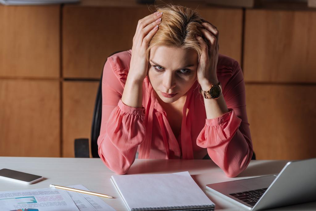 Mujer frustrada sosteniendo la cabeza y sentada a la mesa en la oficina
 - Foto, imagen