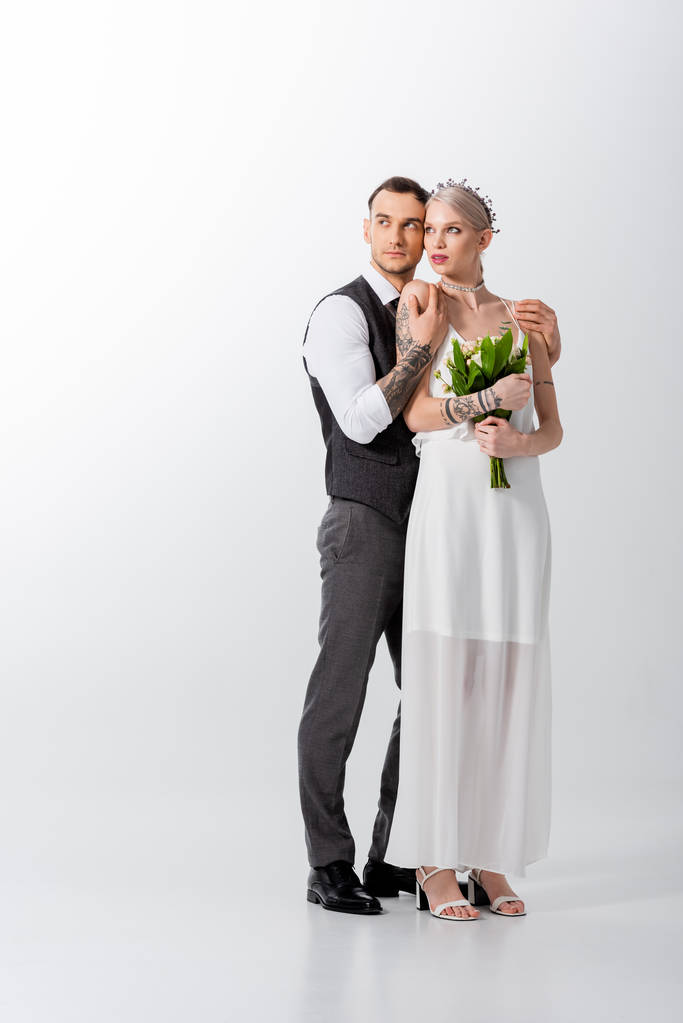 krásná tetovaná nevěsta a pohledný ženich objímající na bílém - Fotografie, Obrázek