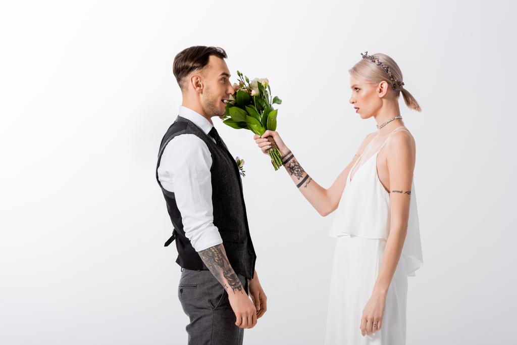 boční pohled na krásné tetované nevěsty bít s kyticí pohledný ženich izolované na bílém - Fotografie, Obrázek