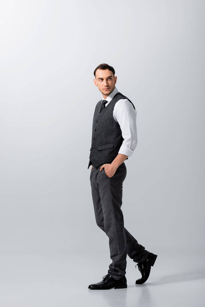 guapo tatuado elegante novio caminando con las manos en bolsillos sobre fondo gris
 - Foto, imagen