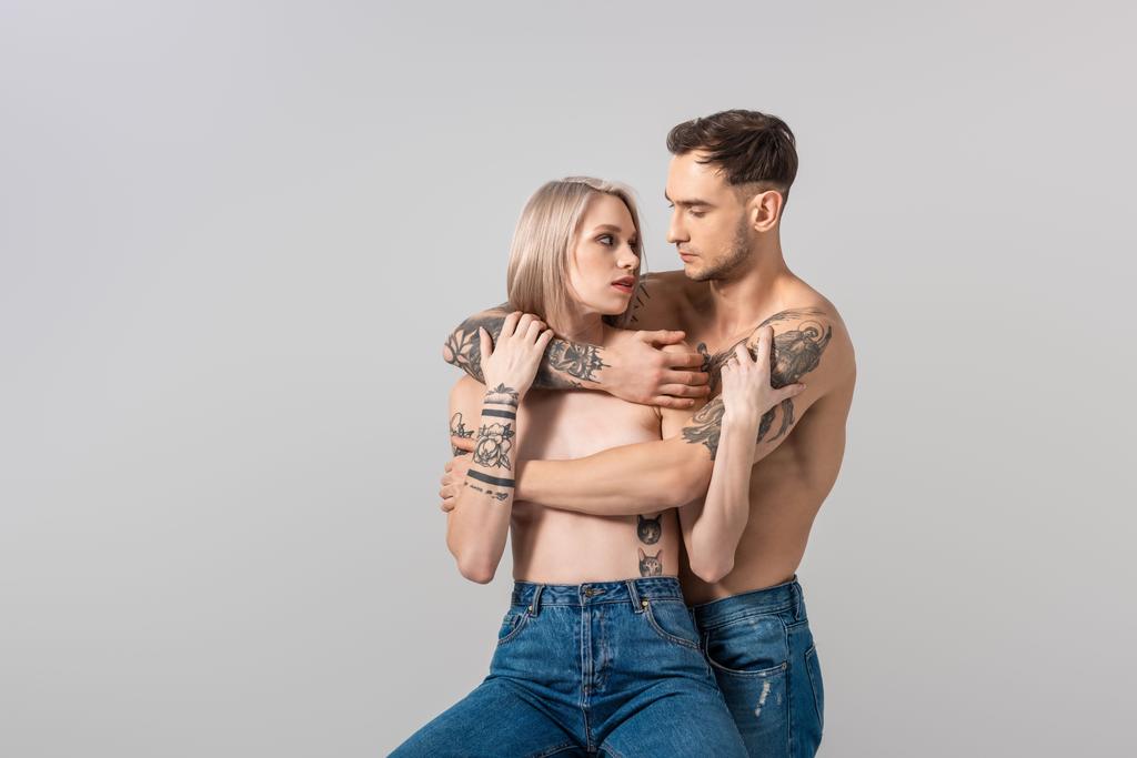 giovane coppia tatuata senza maglietta in jeans che si abbraccia isolata sul grigio
 - Foto, immagini