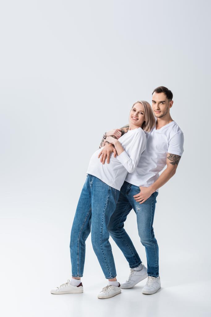 šťastný mladý tetovaný těhotná žena s manželem na šedé - Fotografie, Obrázek