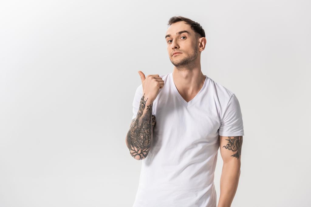 όμορφος νεαρός με τατουάζ που δείχνει με το δάχτυλο στην άκρη απομονωμένος στα λευκά - Φωτογραφία, εικόνα