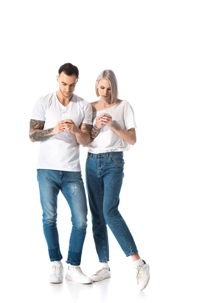 νεαρό ζευγάρι με τατουάζ που χρησιμοποιεί smartphones απομονωμένα σε λευκό - Φωτογραφία, εικόνα