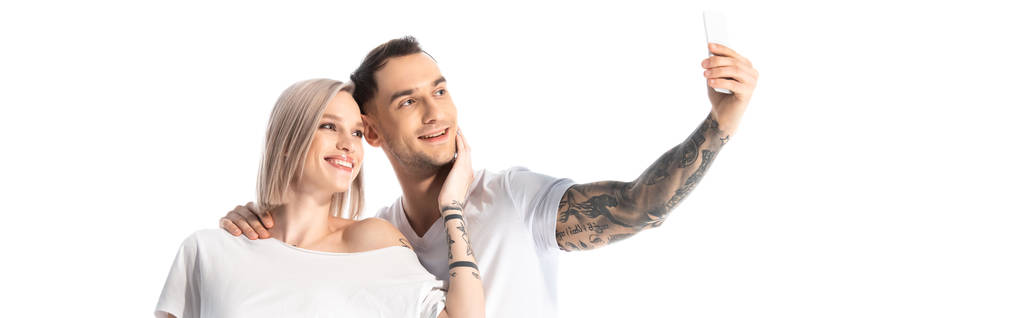 šťastný mladý tetovaný pár přičemž selfie izolované na bílém, panoramatický výstřel - Fotografie, Obrázek