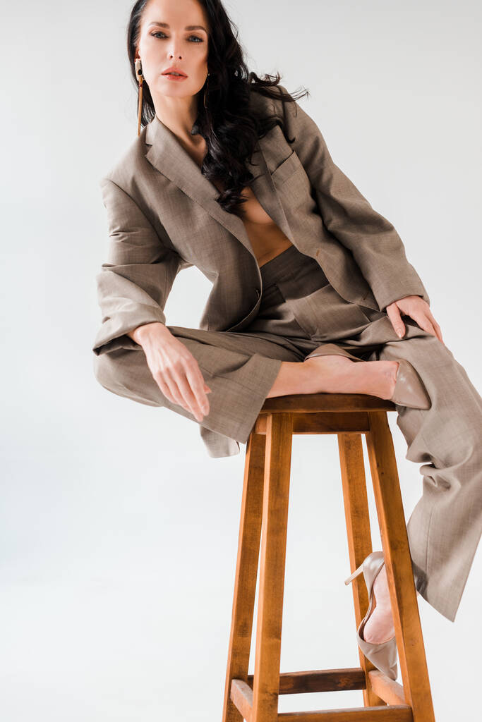mujer sexy y elegante en traje sentado en el taburete sobre fondo gris
  - Foto, Imagen