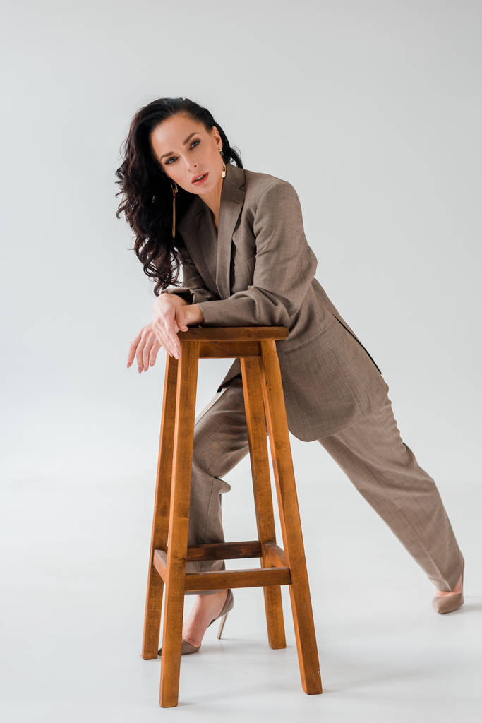 stylish woman in suit on stool looking at camera on grey background  - Photo, Image