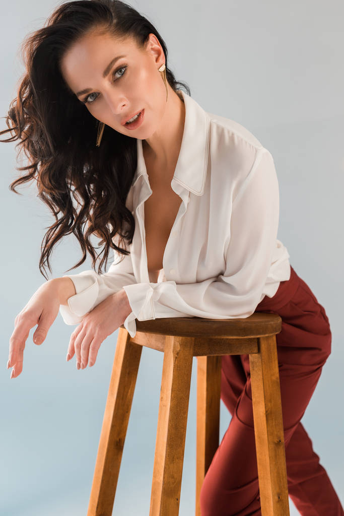 aantrekkelijke en sexy vrouw in shirt en broek op zoek naar camera geïsoleerd op grijs  - Foto, afbeelding