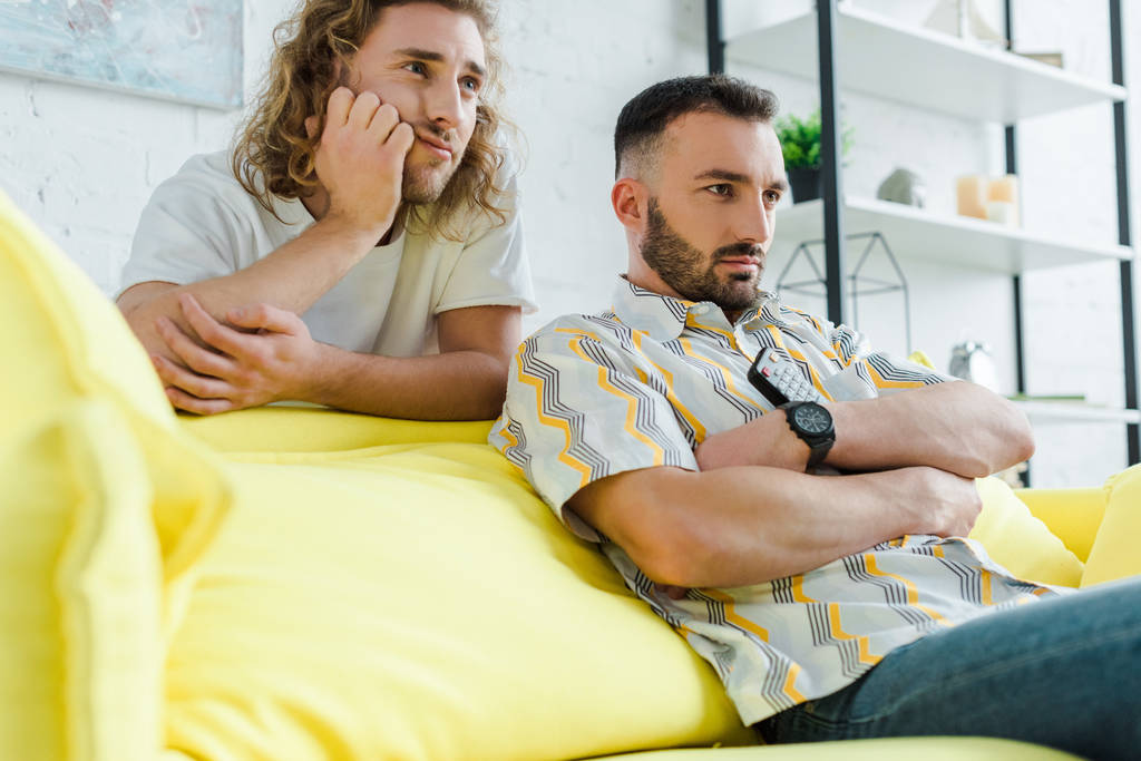 Selektiver Fokus unzufriedener homosexueller Männer, die sich Film im Wohnzimmer ansehen  - Foto, Bild