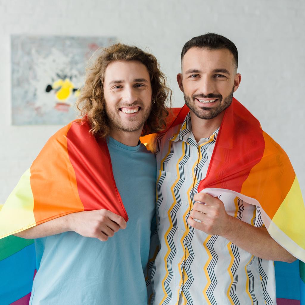 fröhliche homosexuelle Männer mit lgbt-Fahne und Blick in die Kamera  - Foto, Bild