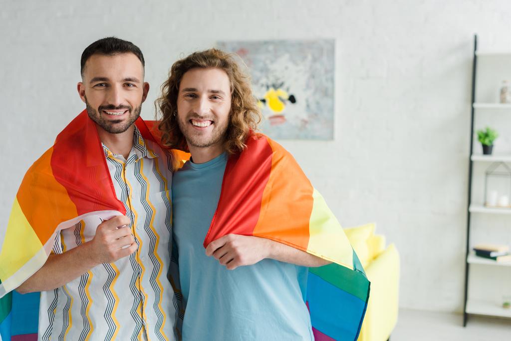 Ευτυχισμένοι ομοφυλόφιλοι άντρες με σημαία lgbt και κοιτάζοντας την κάμερα  - Φωτογραφία, εικόνα