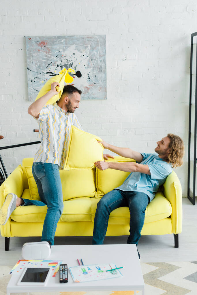 perfil de homens homossexuais felizes travesseiro lutando na sala de estar
  - Foto, Imagem