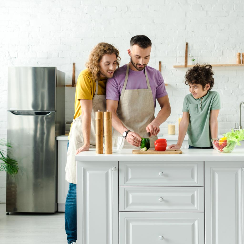 heureux mixte race enfant près beau homosexuel parents cuisine dans la cuisine
  - Photo, image