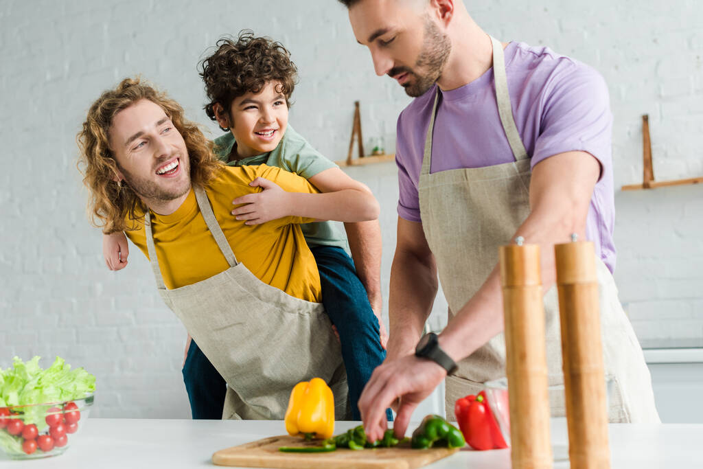 feliz homosexual padre piggybacking mixta raza hijo cerca pareja cocinar en casa
  - Foto, Imagen