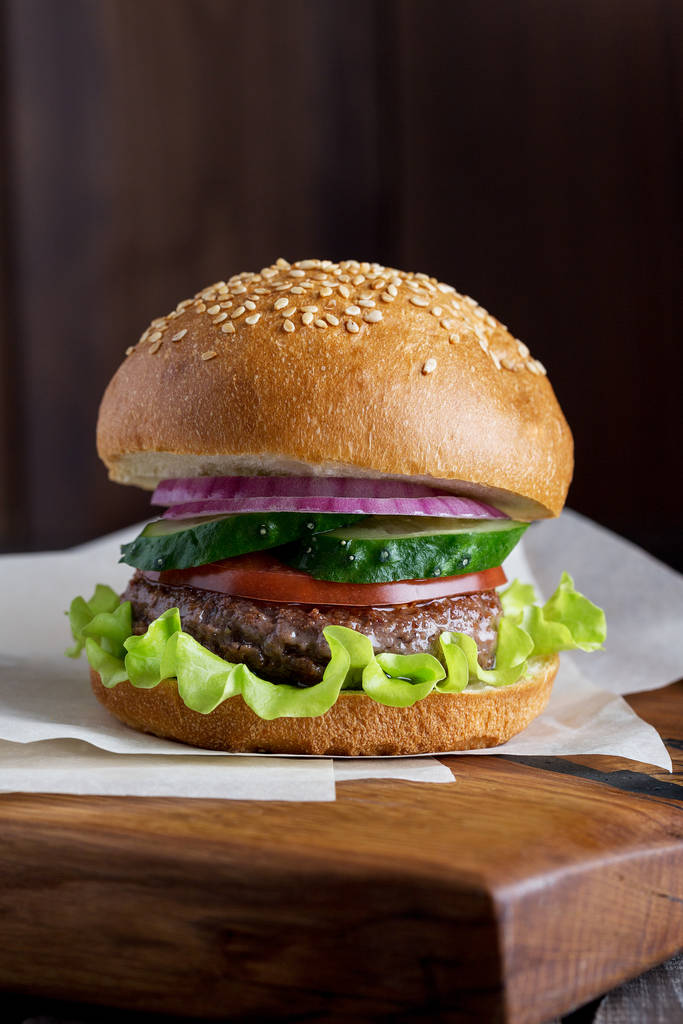 Closeup of home made beef burgers with lettuce served on little wooden cutting board. Dark background - Photo, Image