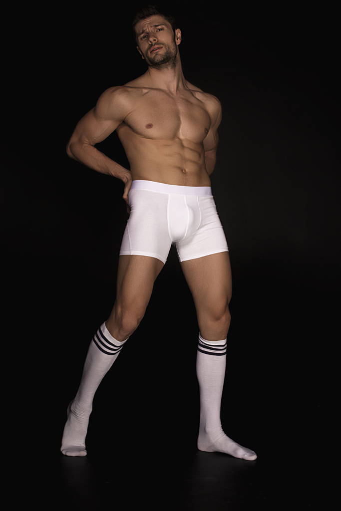 Modelo masculino muscular desnudo fuerte en ropa interior blanca y calcetines largos blancos con tiras sobre fondo de fuente aislado negro
 - Foto, imagen