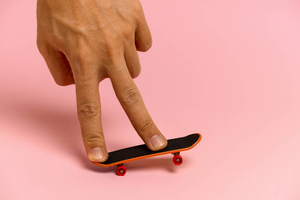рука молодого человека на мини скейтборде на розовом фоне
 - Фото, изображение