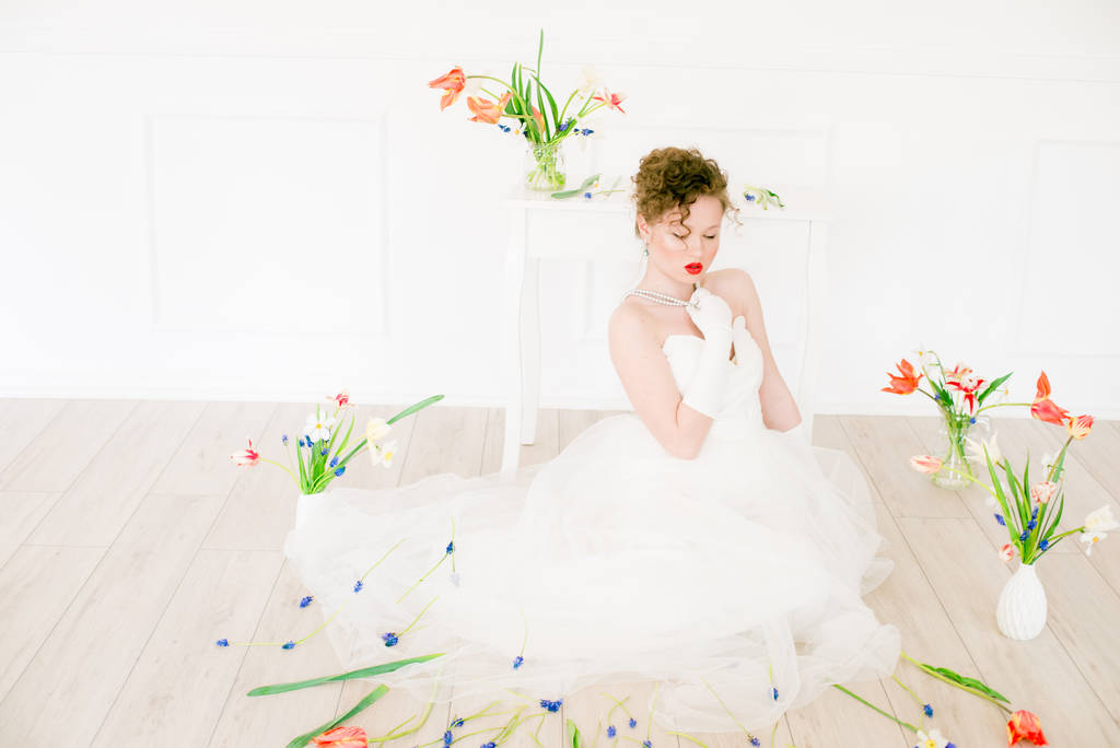 Jolie jeune mariée en robe blanche dans un studio de printemps léger décoré de tulipes. Beauté et mode
 - Photo, image