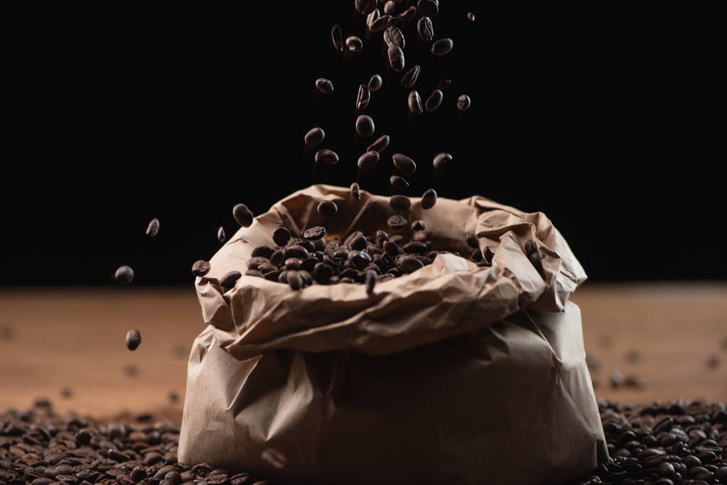 gebrande koffiebonen vallen in zak op zwarte achtergrond - Foto, afbeelding