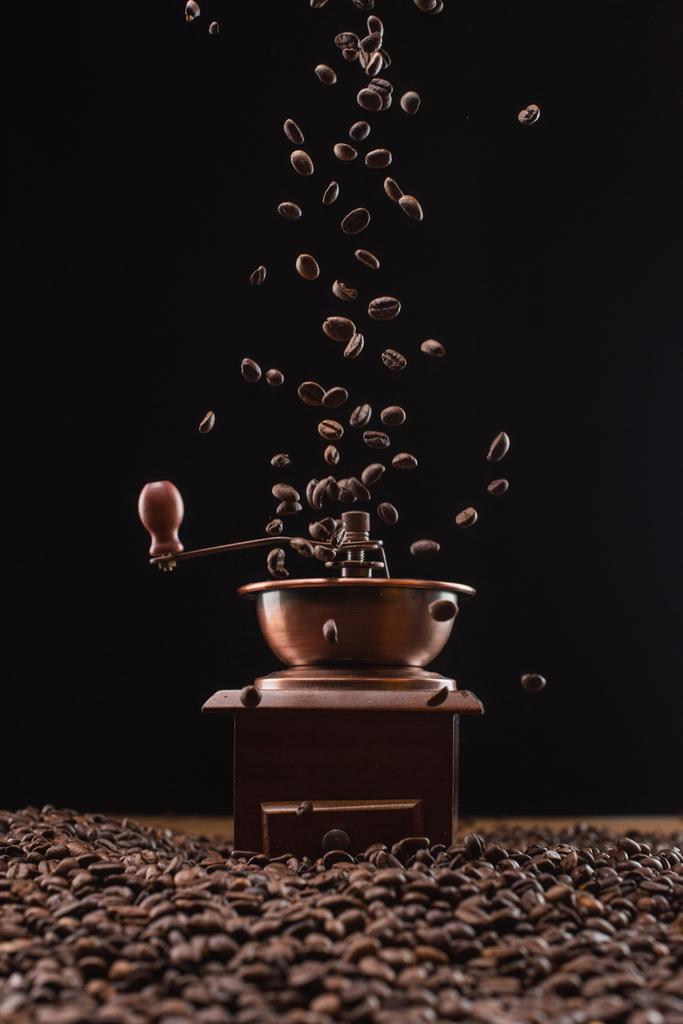 molinillo de café y granos de café tostados frescos en el aire aislado en negro
 - Foto, imagen