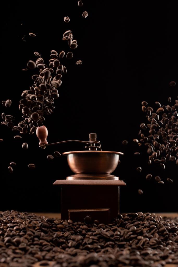 μύλος καφέ και φρέσκοι καβουρδισμένοι κόκκοι καφέ στον αέρα απομονωμένοι σε μαύρο - Φωτογραφία, εικόνα