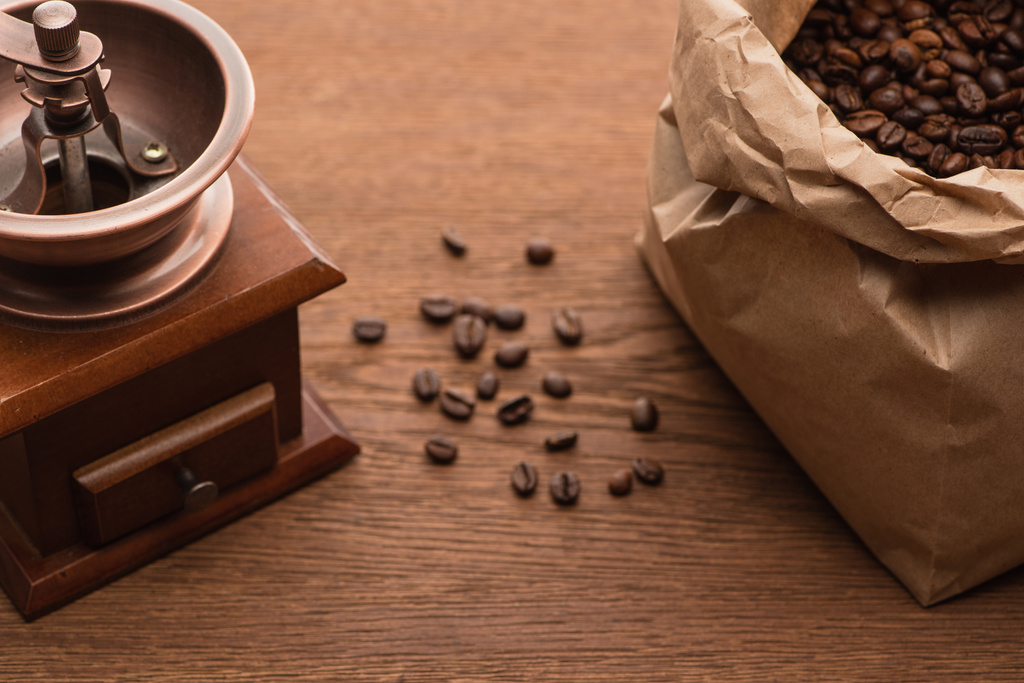 enfoque selectivo de granos de café tostados frescos en bolsa de papel cerca de molinillo de café en la mesa de madera
 - Foto, imagen