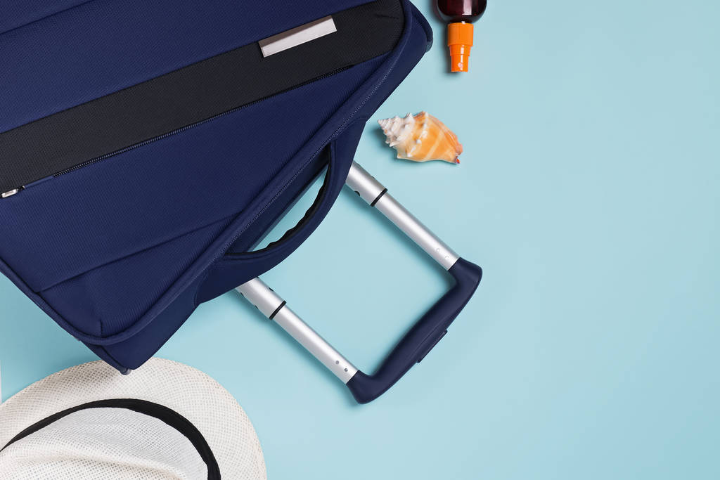 夏休みの平らなレイアウト。スーツケース、パスポート、帽子の青い背景にコピースペース - 写真・画像