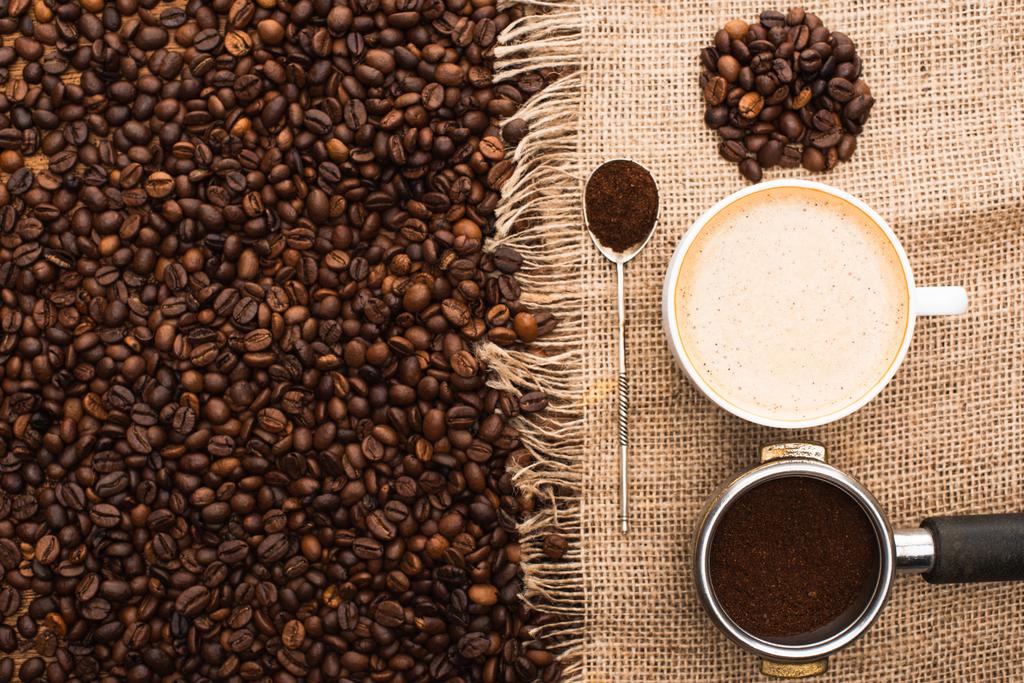 vue du dessus des grains de café frais torréfiés et sac avec cappuccino, cuillère et porte-filtre avec café moulu
 - Photo, image