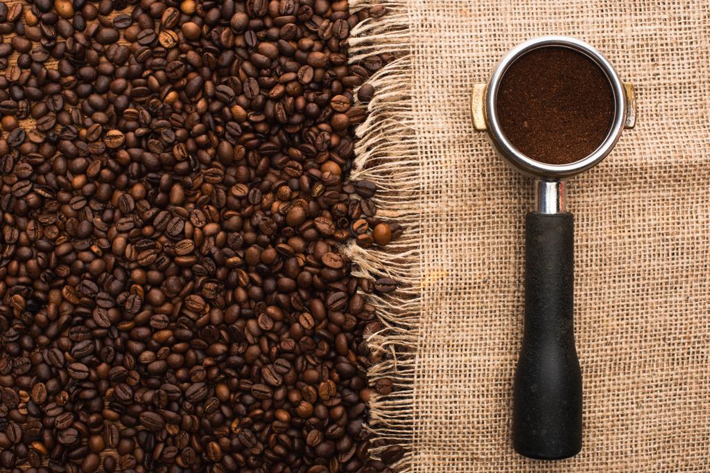 vrchní pohled na čerstvě pražená kávová zrna a držák na filtry s mletou kávou na pytlovině - Fotografie, Obrázek