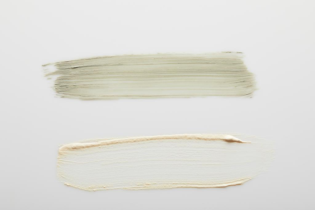 Gri arkaplanda kozmetik kil ve ton kremi fırça darbelerinin üst görünümü - Fotoğraf, Görsel