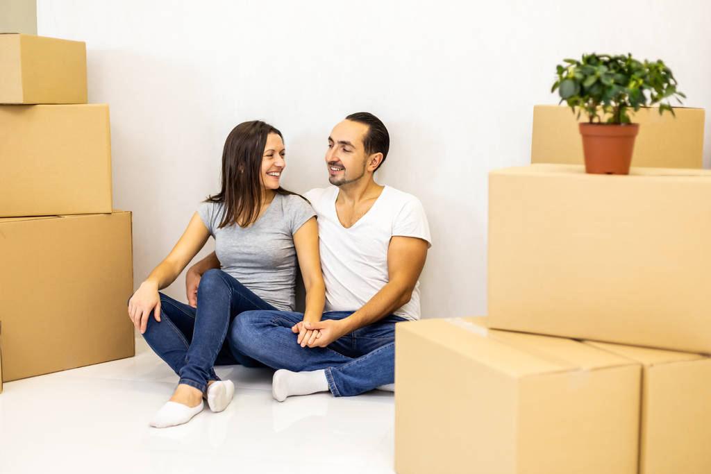 Verpakt en klaar om in een nieuw huis te gaan wonen. Opgewonden jonge echtgenoten zitten tussen kartonnen dozen klaar om te verhuizen. - Foto, afbeelding