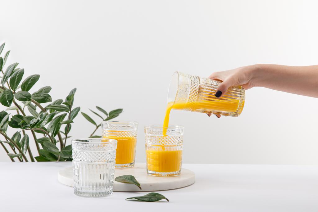 cropped view of woman pouring delicious yellow smoothie in glass on white surface near green plant - Photo, Image
