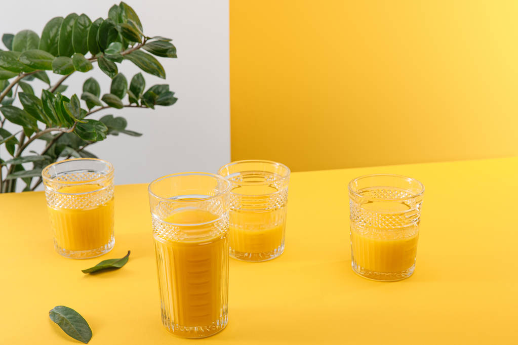 склянки свіжої смачної жовтої смузі біля зеленої рослини
 - Фото, зображення