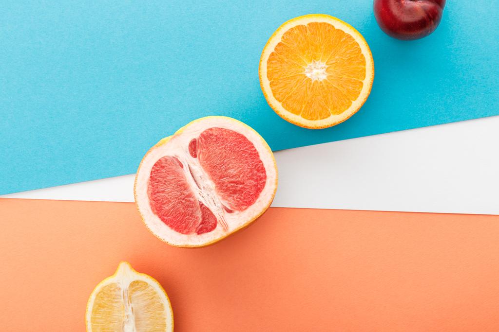 Вид зверху на половинки фруктів і яблуко на синьому, помаранчевому і білому тлі
 - Фото, зображення