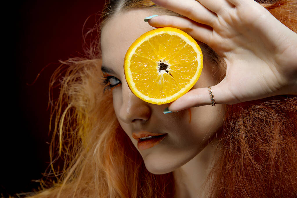 オレンジ色の果実を持つ美しい赤毛の女の子  - 写真・画像