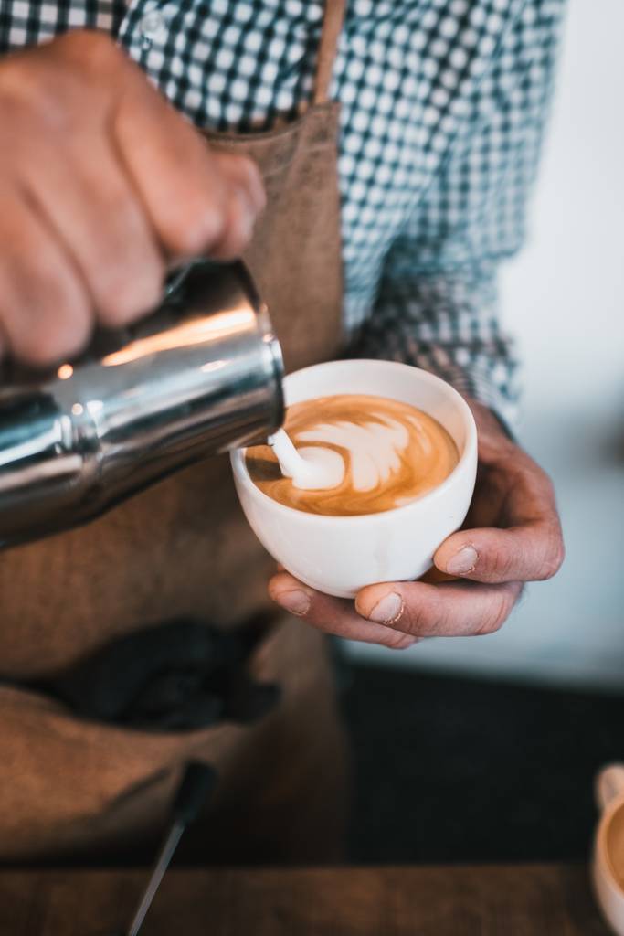 Eine vertikale Aufnahme eines Mannes, der in einem Café Milch in eine Cappuccino-Tasse gießt - Foto, Bild