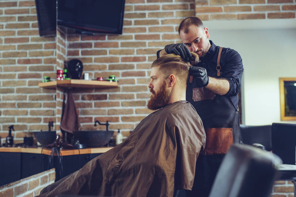 Új frizurát hoz létre. Fiatal szakállas férfi hajvágás fodrász. - Fotó, kép