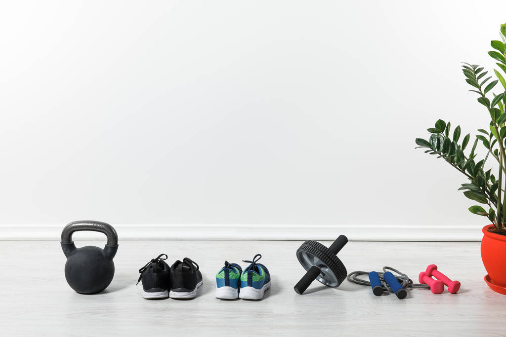 sport shoes, skipping rope, abdominal wheel and kettlebell on floor at home  - Photo, Image