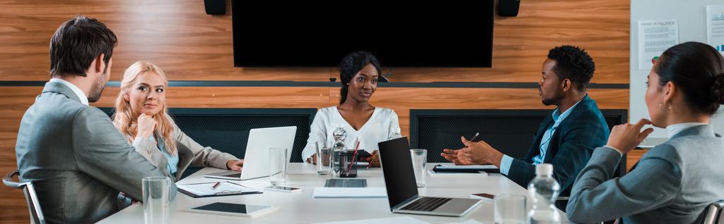 panoramiczne ujęcie młodych wielokulturowych biznesmenów rozmawiających podczas posiedzenia w sali konferencyjnej - Zdjęcie, obraz
