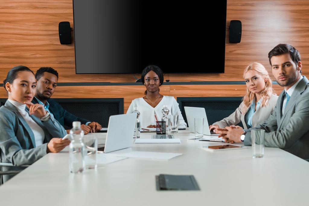 jóvenes y seguros empresarios multiculturales sentados en la sala de conferencias con pantalla LCD en la pared
 - Foto, Imagen