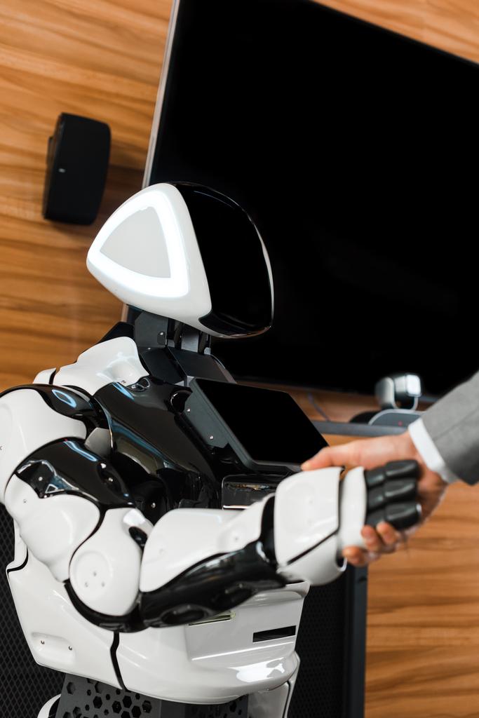 visão parcial do empresário apertando as mãos com robô humanoide no escritório
 - Foto, Imagem