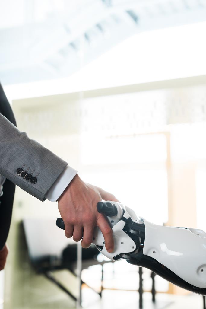 vista parcial del hombre de negocios y robot estrechando la mano en la oficina
 - Foto, Imagen