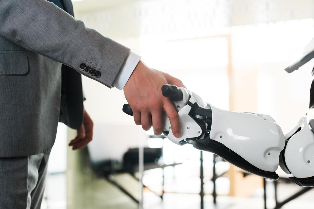 abgeschnittene Ansicht von Geschäftsmann und Roboter beim Händeschütteln im Büro - Foto, Bild
