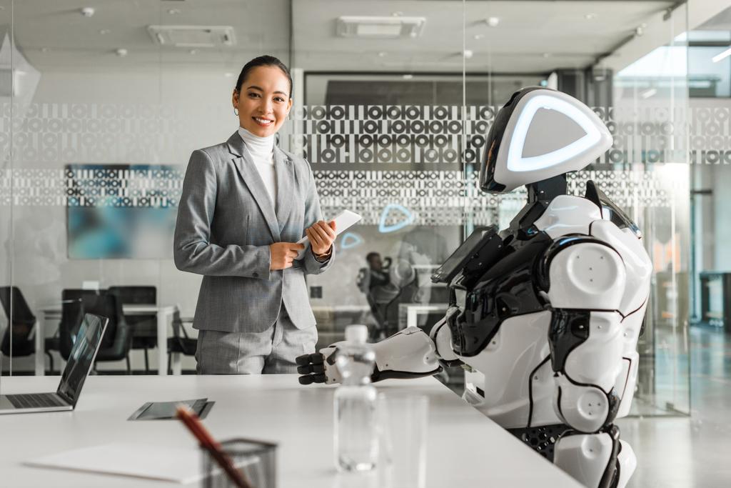 会議室でロボットのそばに立ちながらデジタルタブレットを持っているアジアの女性の笑顔 - 写真・画像