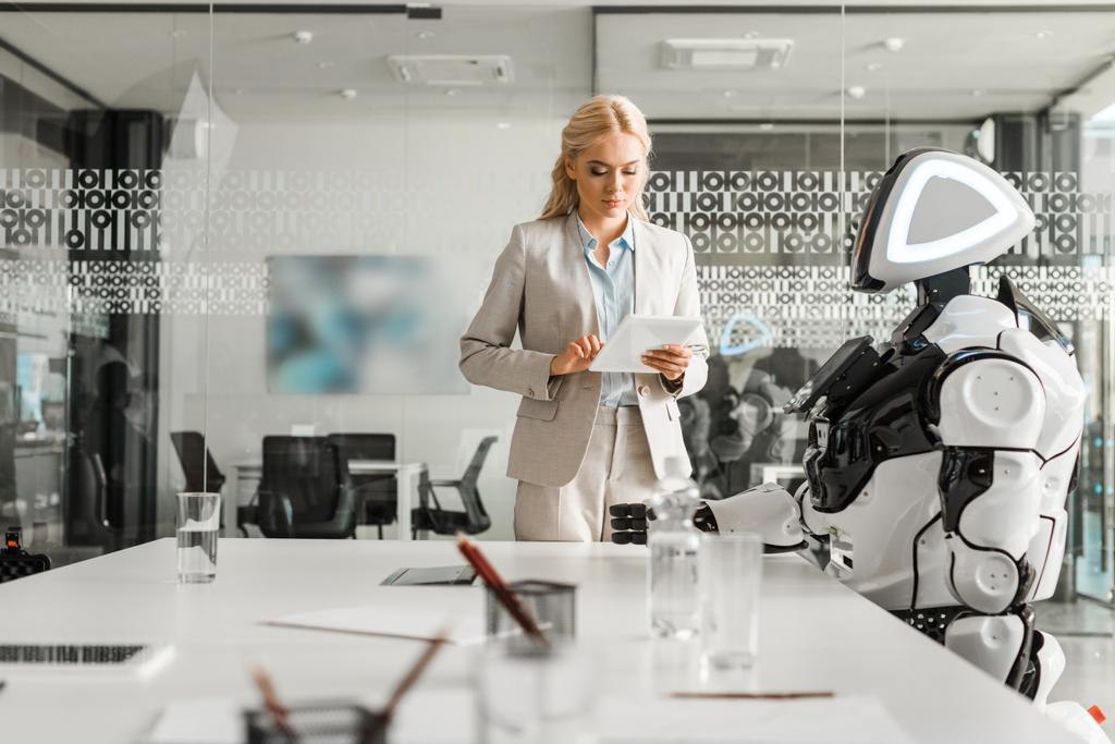 会議室でロボットのそばに立ちながらデジタルタブレットを使う魅力的なビジネスウーマン - 写真・画像