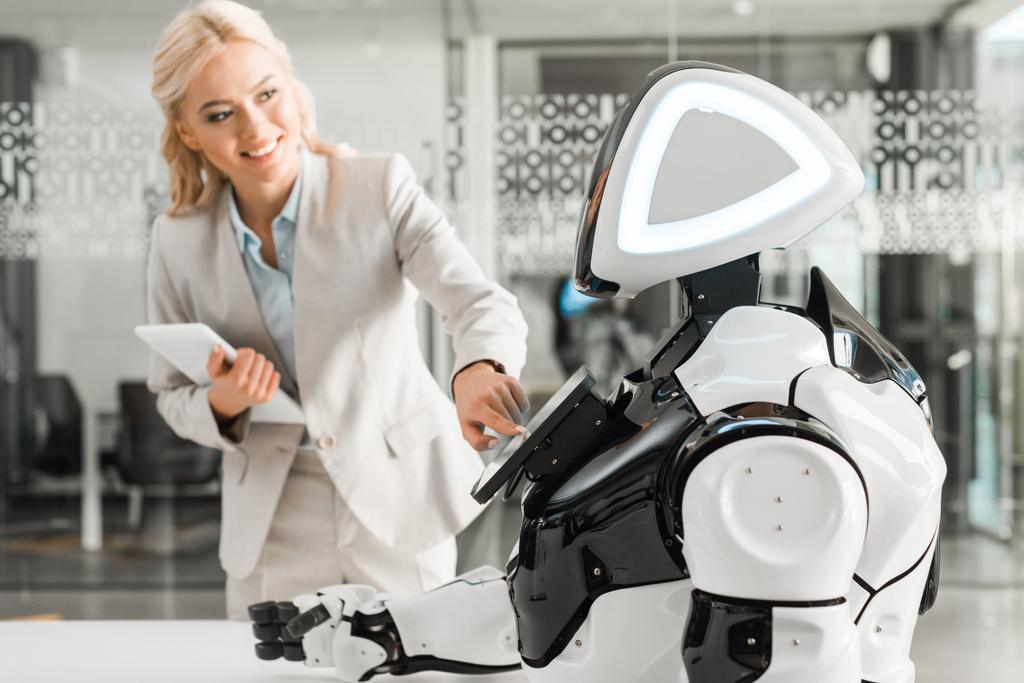 Lächelnde Geschäftsfrau bedient Roboter mit digitalem Tablet - Foto, Bild