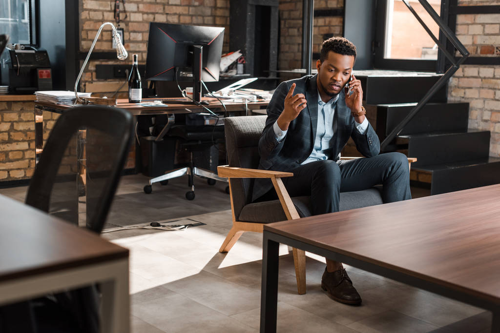 komoly afro-amerikai üzletember ül karosszékben, és bemutatja ötlet gesztus, miközben beszél az okostelefon - Fotó, kép